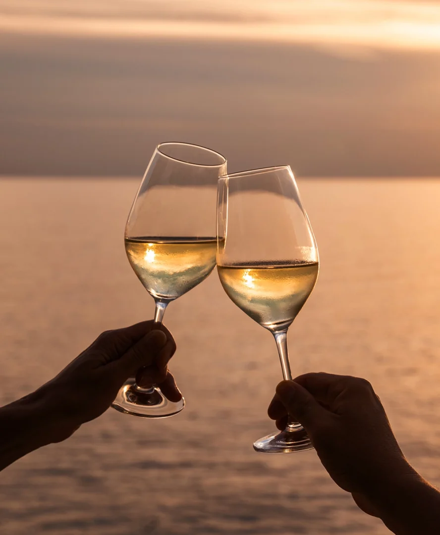 Anstoßen mit Weißwein bei Sonnenuntergang über dem Meer